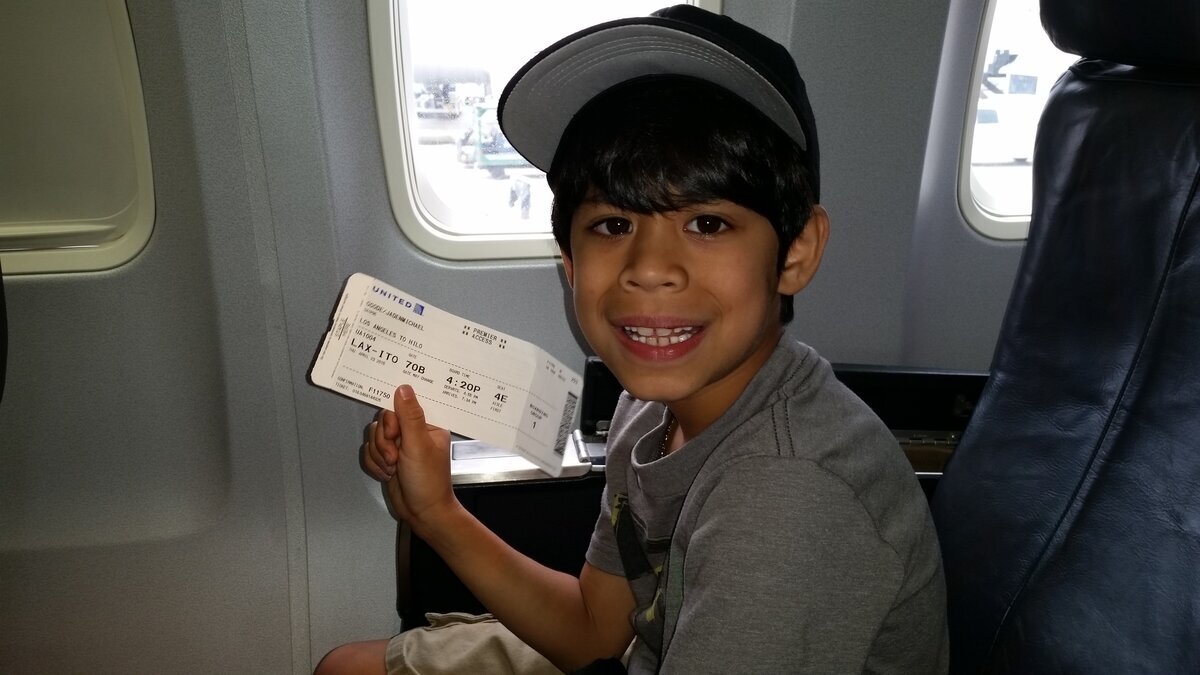 Young Jaden on plane holding boarding pass with big smile