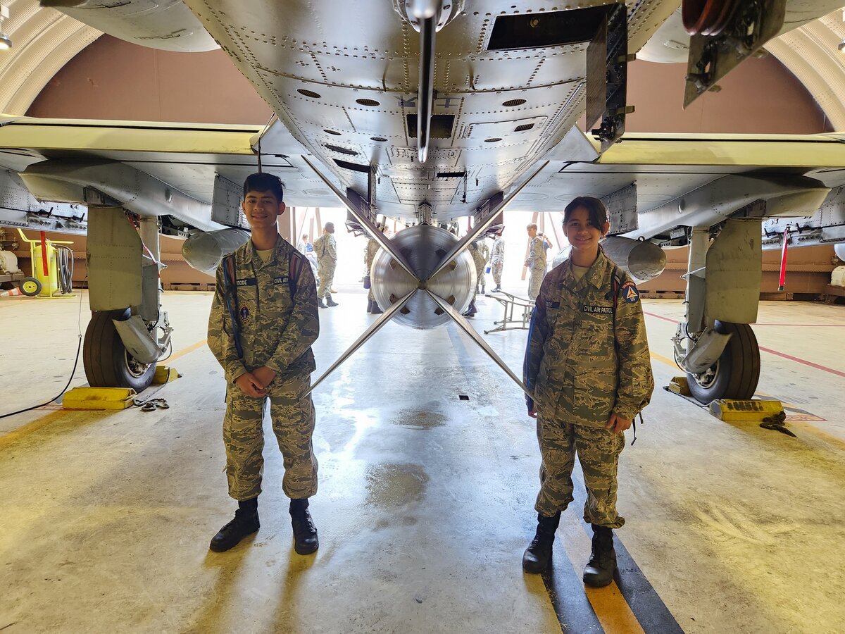 Two cadets standing under massive military aircraft